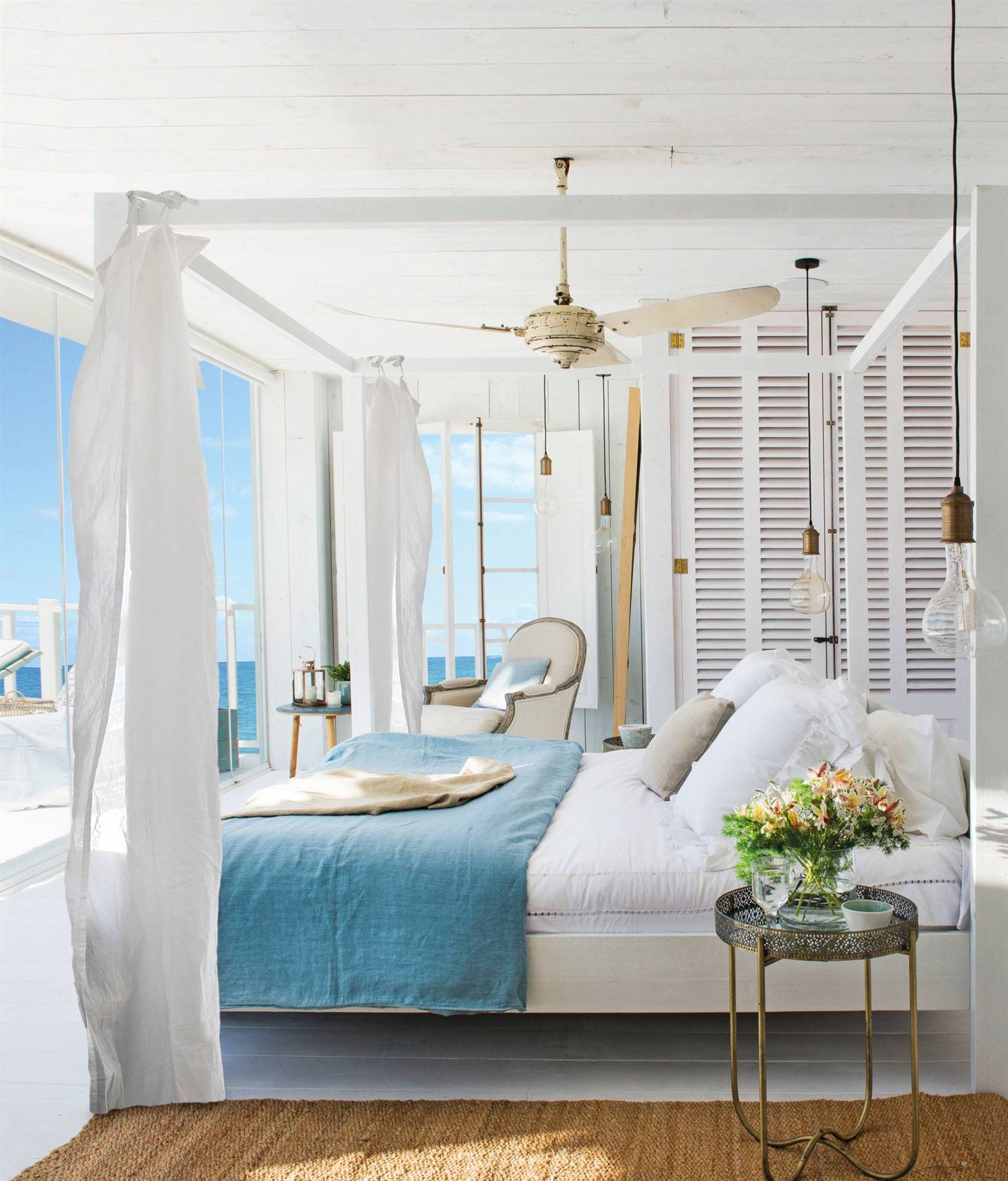 Large white summerhouse bedroom with four-poster bed, blue accents, and sea views 00461872
